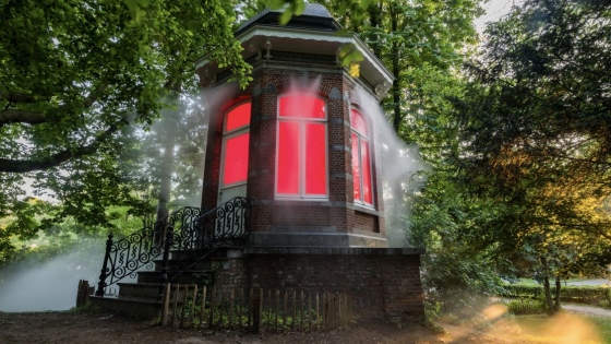 Afbeelding van kapelletje in een park dat rook uitstoomt en rood verlicht is vanbinnen