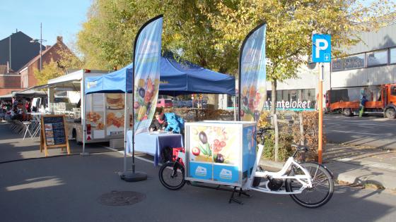 Wevelgemse fietskoeriers - standplaats met blauwe tent en vlaggen en buiten een blauwe bakfiets met reclame