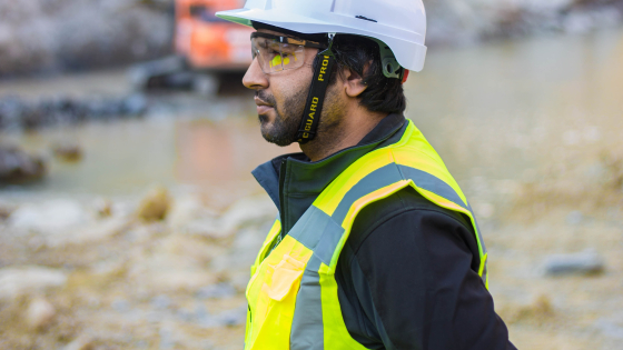 bouwvakker in uitrusting met witte helm en geel hesje en beschermglazen is bezig on the job