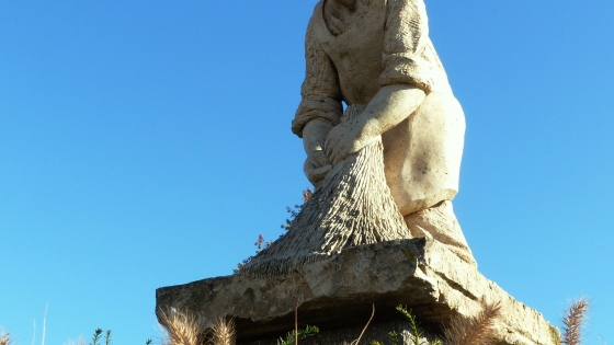 Foto van een kunstwerk van Michel Samyn. De Vlasser is een standbeeld middenin het vlas en het beeld iemand af die het vlas ophaalt