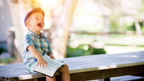 Lachend kindje op een bank met een boek in zijn handen 