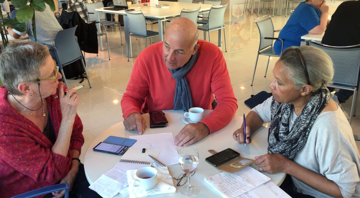 Drie mensen zitten met hun smartphones aan een tafel en praten over digitale problemen