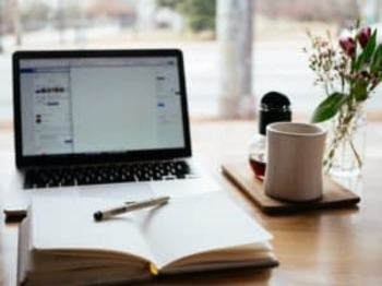 het online boekprogramma Wise met een laptop en daarvoor een open boek en ernaast een kop koffie